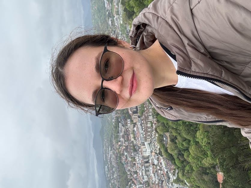 Iana Perovich outdoors, with a city and green hills behind her